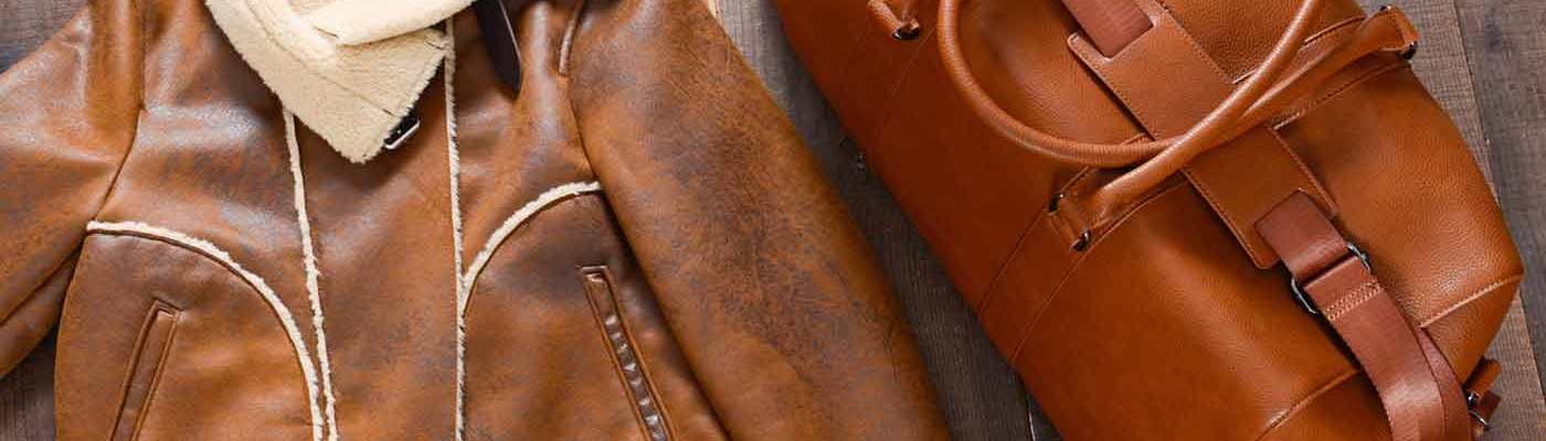 A brown leather jacket lined with sheepskin and a leather bag lie on a wooden floor.